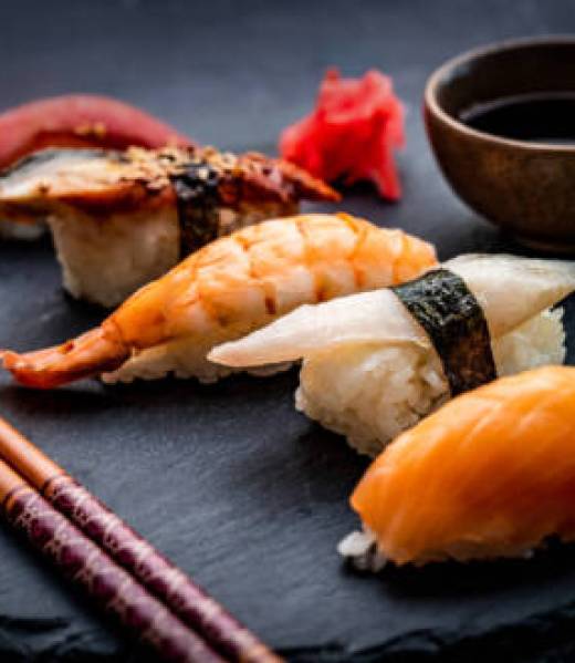 Tasty sushi sashimi set composition with shrimps, ginger and soy sauce served with chopsticks and green wasabi on black round plate. Traditional asian food with rice and seafood